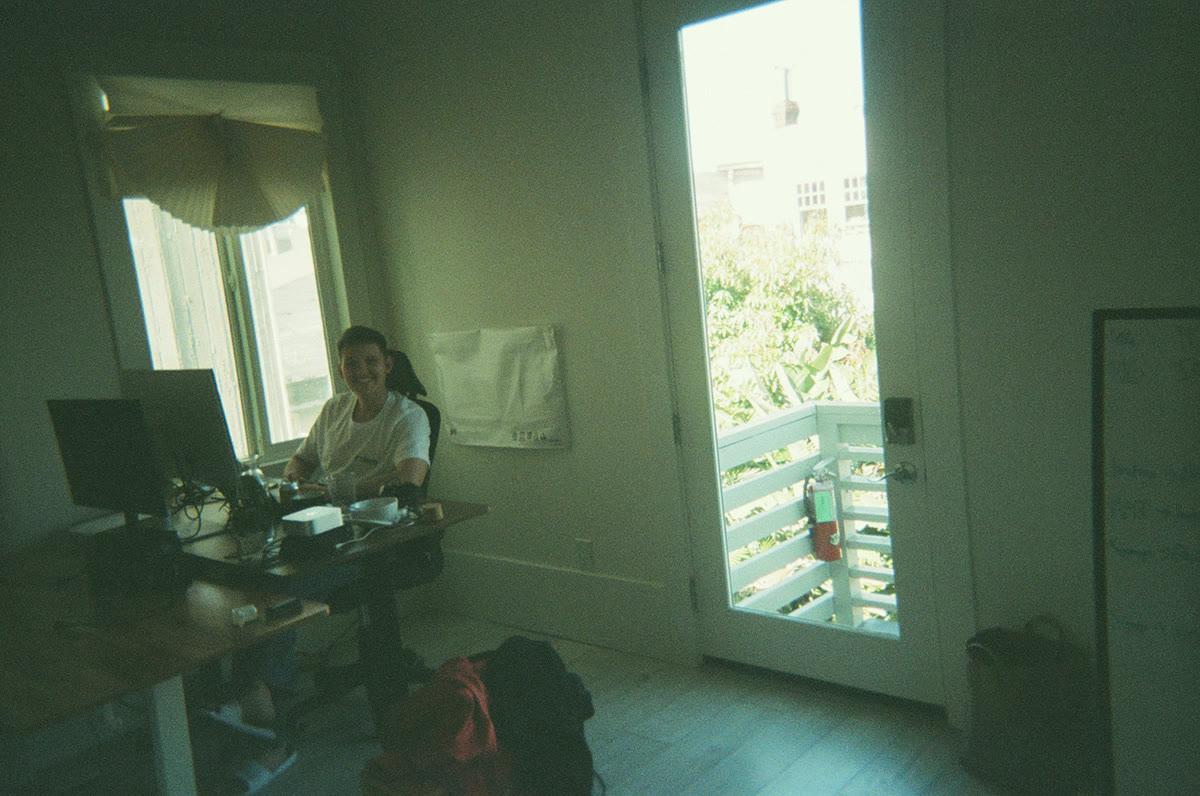 A teammate at a desk in the San Francisco house, the balcony door open beside her
